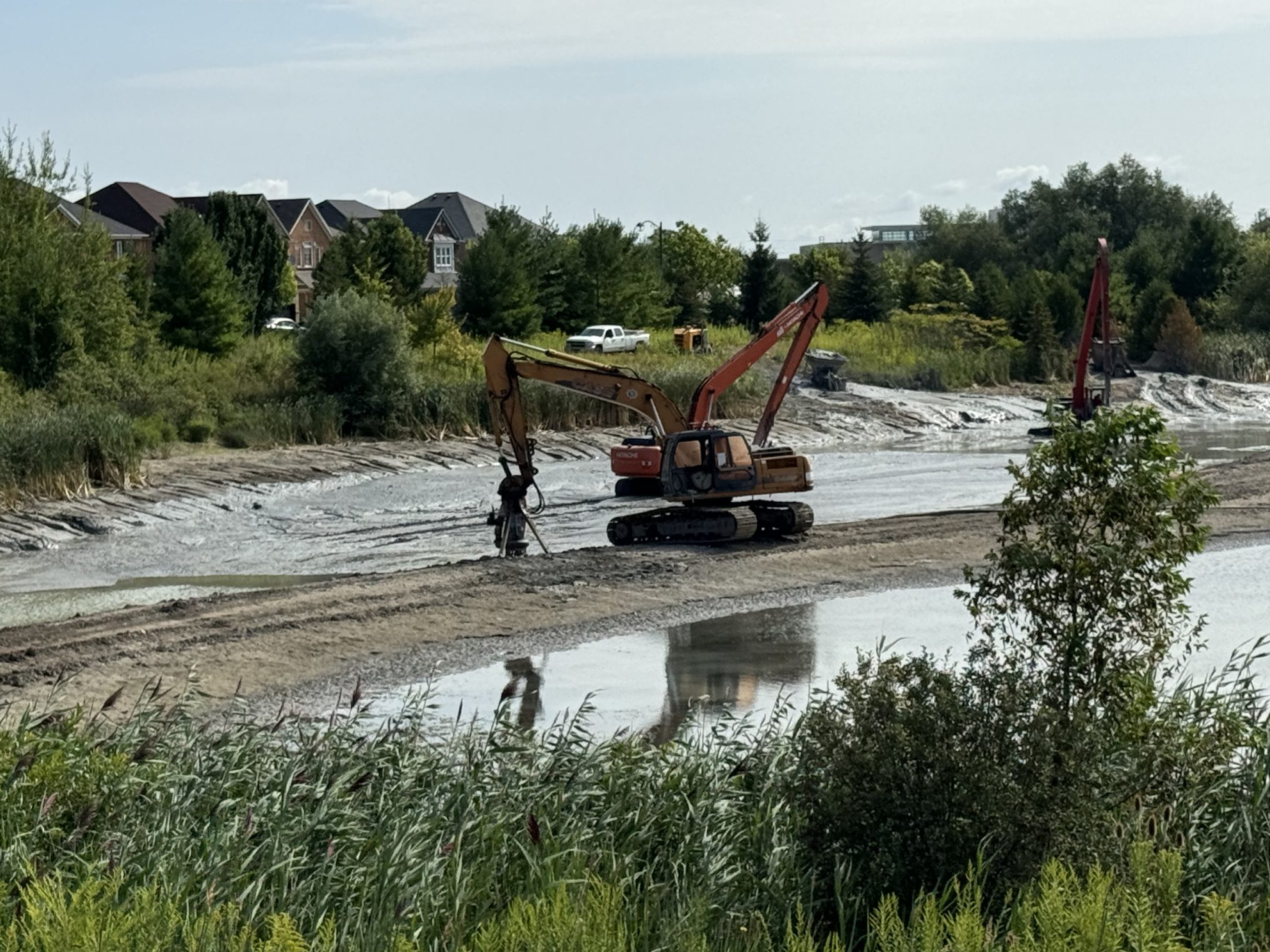 Excavators dredging muddy pond near suburban houses