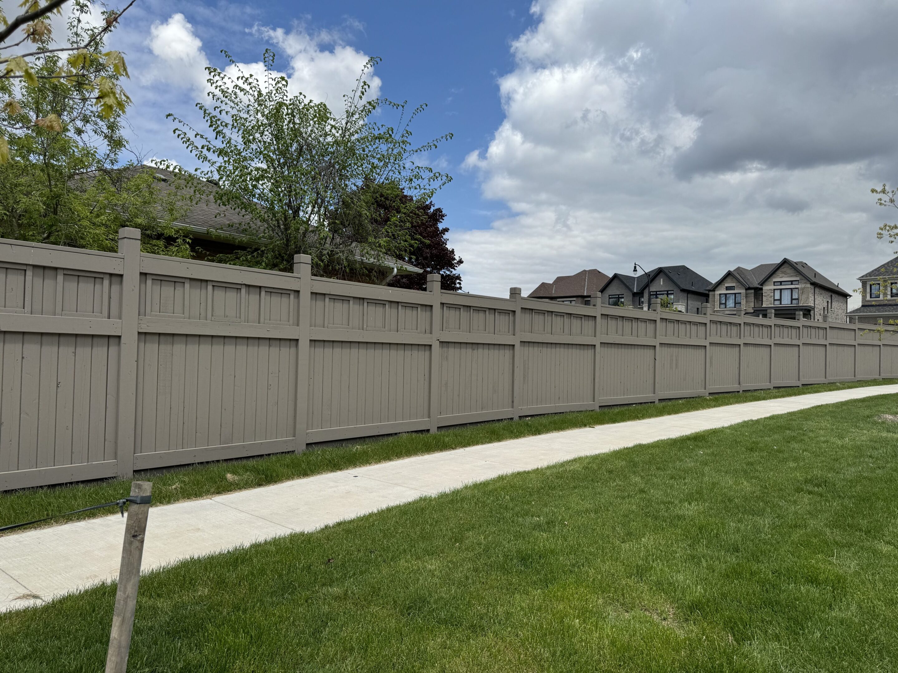 Suburban sidewalk alongside tall beige wooden fence
